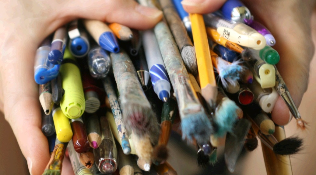 Dorene's hands filled with pencils, pens, paint brushes and markers