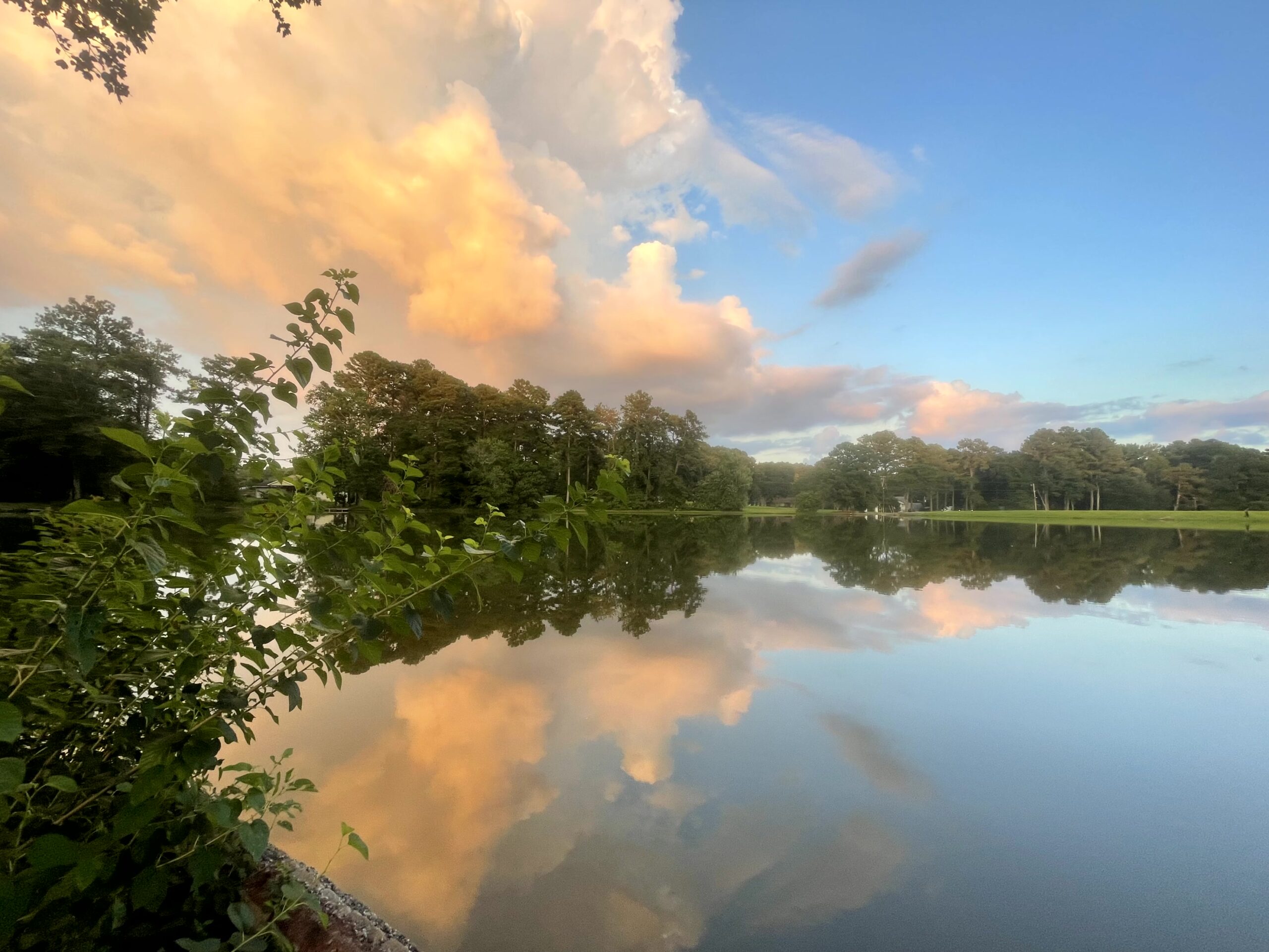 blue sky with pinkish orange clouds above green trees all reflected in a lake